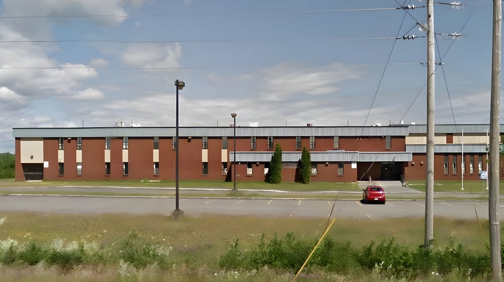 Das mehrstöckige Backsteingebäude der Botwood Collegiate mit einem roten Auto im Vordergrund ist von einer Wiese umgeben.