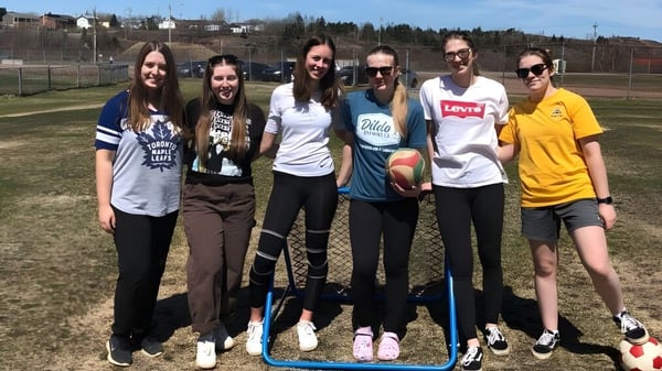 Eine Gruppe Schülerinnen steht auf einer Wiese vor einem Zaun und Gebäuden auf dem Campus der Botwood Collegiate.