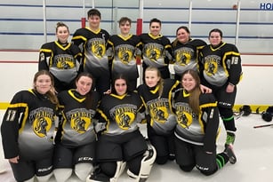 Eine Gruppe von jungen Hockeyspielerinnen der Botwood Collegiate posiert gemeinsam auf der Eisbahn mit dem Schriftzug HOME im Hintergrund.