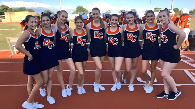 Eine Gruppe junger Schülerinnen in Uniformen steht zusammen auf dem Sportfeld der Boulder Creek High School.
