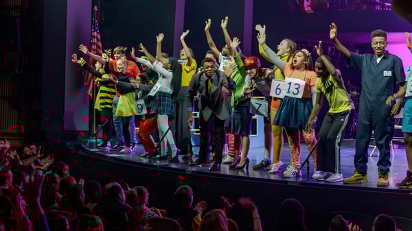 Schüler der Bournemouth Collegiate School zeigen eine lebhafte Bühnenperformance mit erhobenen Armen in einer farbenfrohen Kulisse.