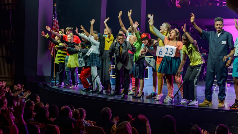 Schüler der Bournemouth Collegiate School zeigen eine lebhafte Bühnenperformance mit erhobenen Armen vor einem farbenfrohen Hintergrund.