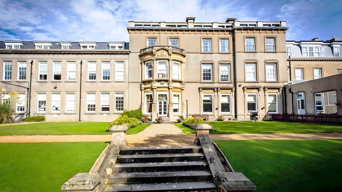 Das prächtige Hauptgebäude der Bournemouth Collegiate School mit gepflegtem Rasen und steinernen Treppen unter blauem Himmel.