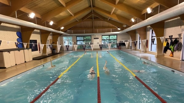 Die Schwimmhalle mit Holzdecke und Bahnenmarkierungen auf dem Campus der Bournemouth Collegiate School mit Schwimmern im Wasser.