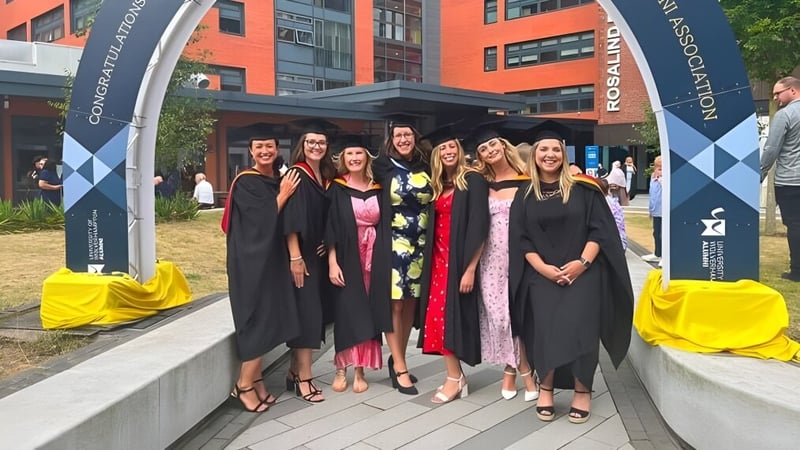 Studierende des Bournemouth & Poole College stehen in Abschlussroben vor einem Universitätsgebäude mit Bannern im Hintergrund.