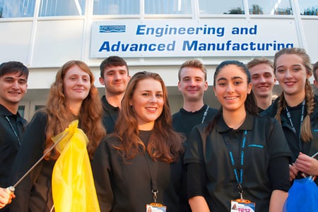 Eine Gruppe Schülerinnen und Schüler in Abschlussroben steht vor dem Gebäude mit dem Schild Engineering and Advanced Manufacturing auf dem Campus des Bournemouth & Poole College.