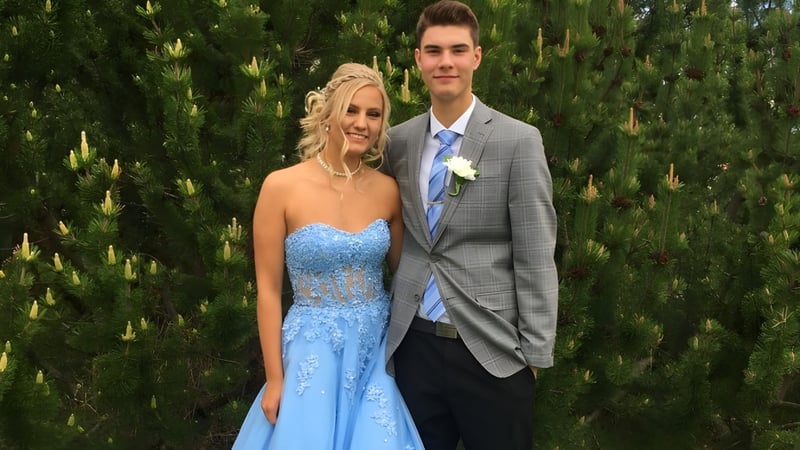 Ein Paar in formeller Kleidung steht vor grünen Bäumen auf dem Gelände der Bowness High School.