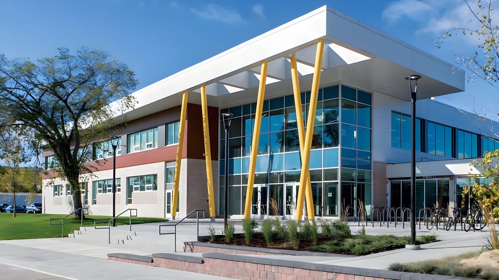 Das moderne, mehrstöckige Gebäude der Bowness High School mit Glas-, weißen und gelben Elementen steht in einer begrünten Umgebung.