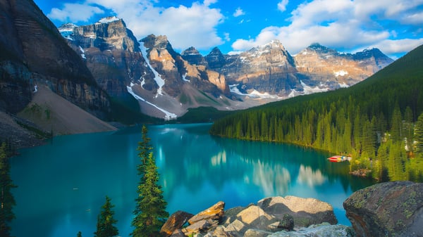Ein ruhiger türkisfarbener See vor schneebedeckten Bergen und einem immergrünen Wald in der Natur nahe der Bowness High School.