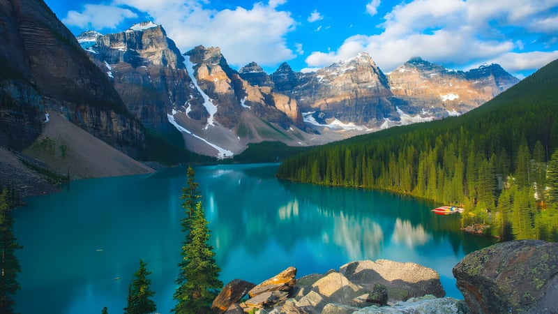Ein ruhiger türkisfarbener See vor schneebedeckten Bergen und einem immergrünen Wald in der Natur nahe der Bowness High School.