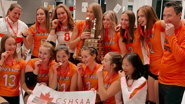 Eine Gruppe junger Sportlerinnen posiert gemeinsam auf dem Gelände der Bowness High School mit einer kanadischen Flagge im Hintergrund.