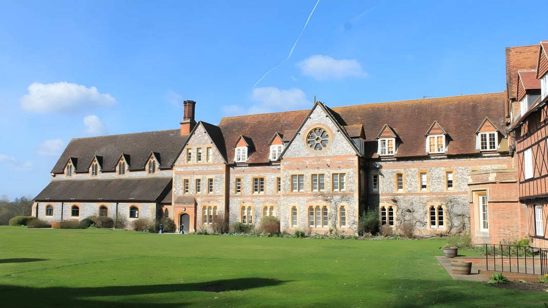 Das historische Backsteingebäude des Bradfield College steht auf einem gepflegten Rasen unter einem blauen Himmel.