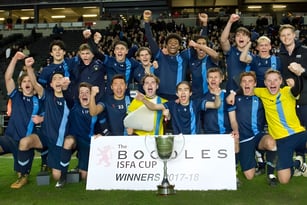 Die Fußballmannschaft des Bradfield College feiert im Stadion mit einem Pokal in der Hand.