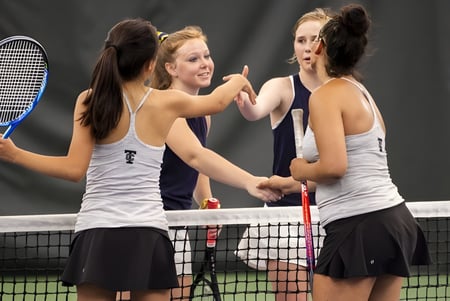 Drei Schülerinnen in Sportkleidung stehen mit Tennisschlägern auf dem Tennisplatz des Braemar College und unterhalten sich.