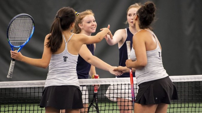 Drei Schülerinnen in Tenniskleidung unterhalten sich auf dem Tennisplatz des Braemar College.