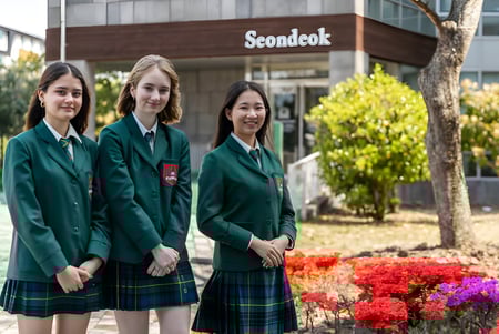 Drei Schülerinnen in grünen Schuluniformen stehen vor dem Gebäude von Branksome Hall Asia.