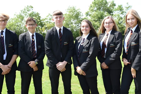 Eine Gruppe von Schülern der Brannel School steht in formeller Kleidung auf einer Wiese mit Bäumen im Hintergrund.
