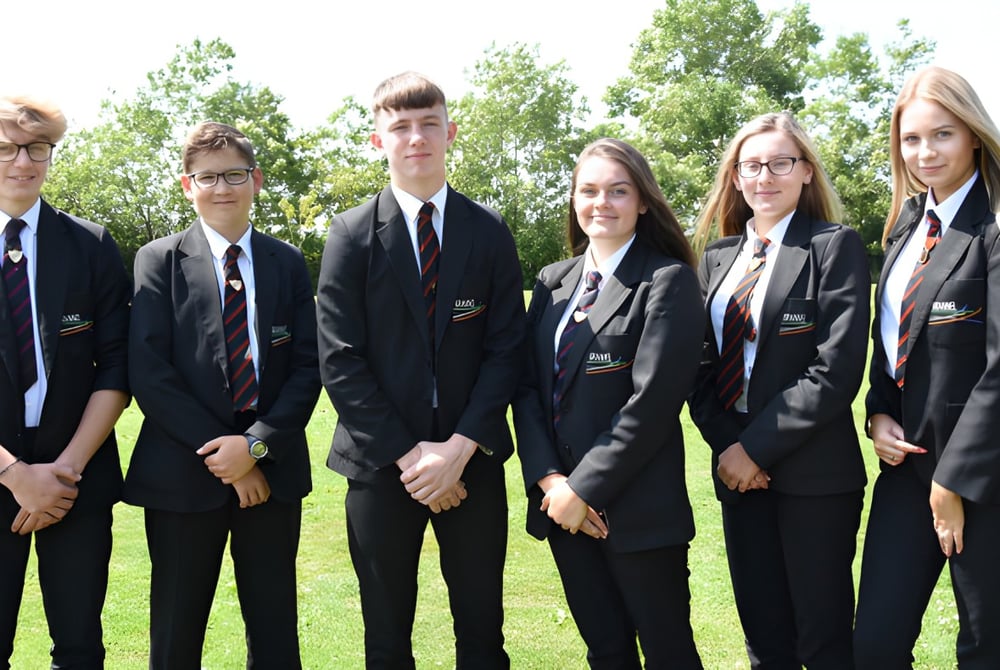 Eine Gruppe von Schülern der Brannel School steht in formeller Kleidung auf einer Wiese mit Bäumen im Hintergrund.