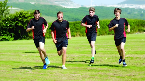 Vier Schülerinnen und Schüler der Brannel School laufen auf einem grasbewachsenen Feld mit Bergen im Hintergrund.
