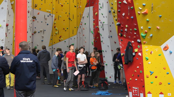 Schüler der Bredon School stehen mit Kletterausrüstung vor einer farbigen Kletterwand in der Kletterhalle.