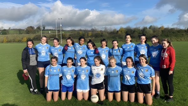 Eine Gruppe junger Fußballspielerinnen des Breifne College steht auf einem Grasfeld unter bewölktem Himmel.