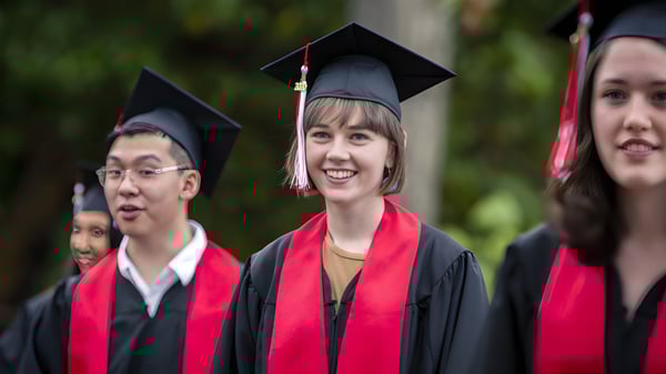 Eine Gruppe von Absolventinnen und Absolventen steht in akademischer Kleidung vor natürlichem Hintergrund auf dem Campus der Brentwood College School.