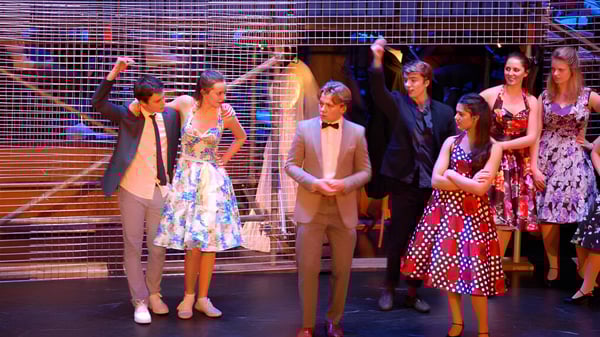 Eine Gruppe Schüler der Brentwood School steht auf einer Bühne mit metallischem Gitter als Hintergrund.