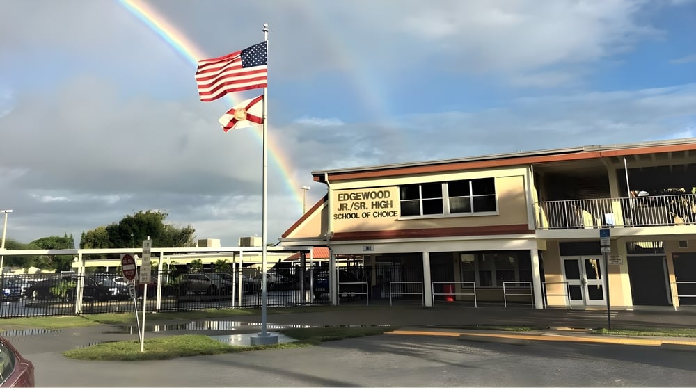Vor dem Schulgebäude der Brevard County Public Schools wehen die amerikanische und eine Bundesstaat-Flagge unter einem Regenbogen am bewölkten Himmel.