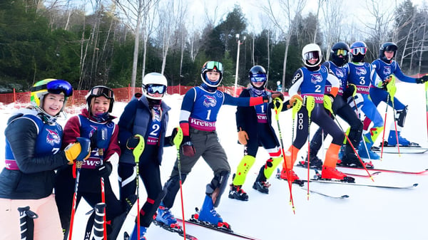 Eine Gruppe von Skifahrern in farbigen Uniformen steht auf einem schneebedeckten Hang auf dem Gelände der Brewster Academy.