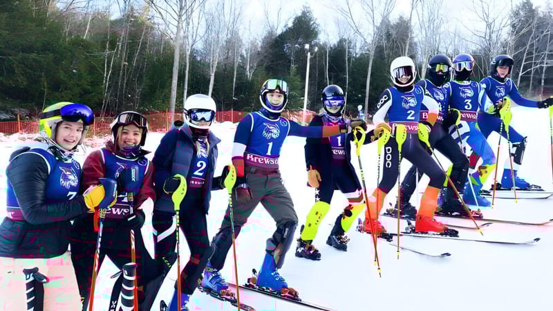 Eine Gruppe von Skifahrern in farbigen Uniformen steht auf einem schneebedeckten Hang auf dem Gelände der Brewster Academy.