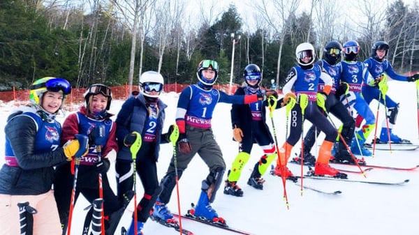 Eine Gruppe von Skifahrern in bunten Uniformen steht auf einem schneebedeckten Hang auf dem Gelände der Brewster Academy.