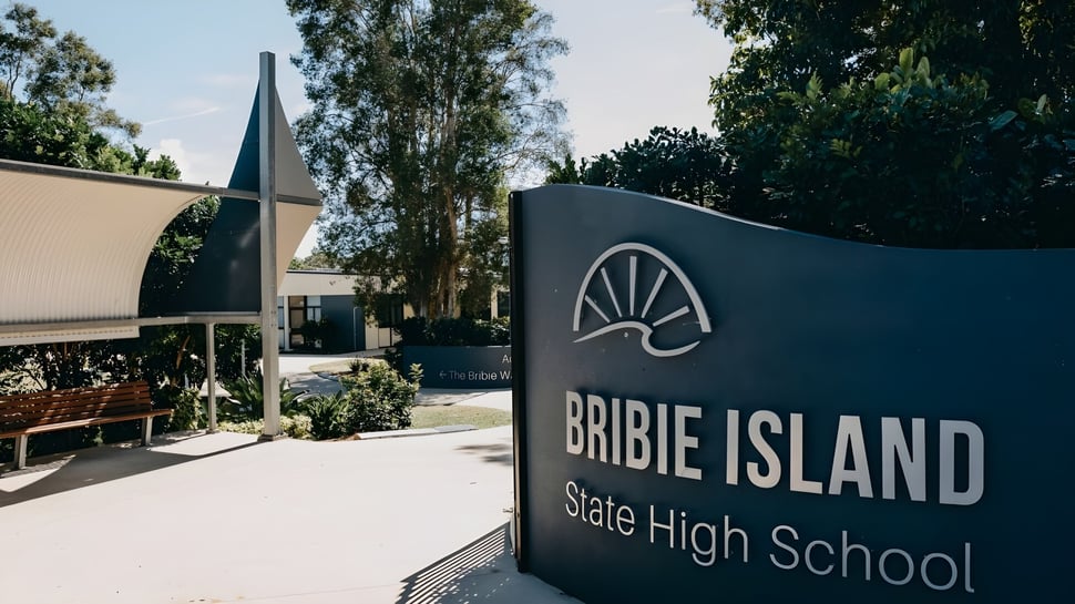 Ein Schild der Bribie Island State High School mit Gebäude und Bäumen im Hintergrund ist zu sehen.
