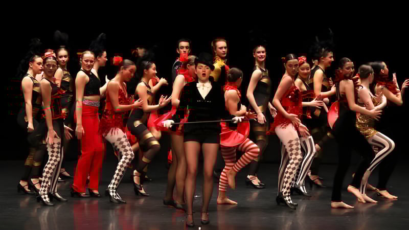 Eine Gruppe von Schülern des Brighton College zeigt eine bunte Bühnenperformance mit farbenfrohen Kostümen auf einer dunklen Bühne.