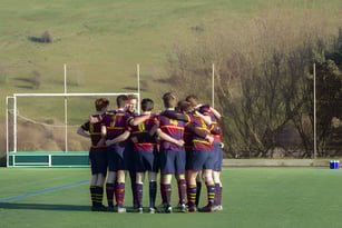 Eine Gruppe von Schülerinnen und Schülern steht auf dem Sportfeld des Brighton College umgeben von einer grünen Landschaft.