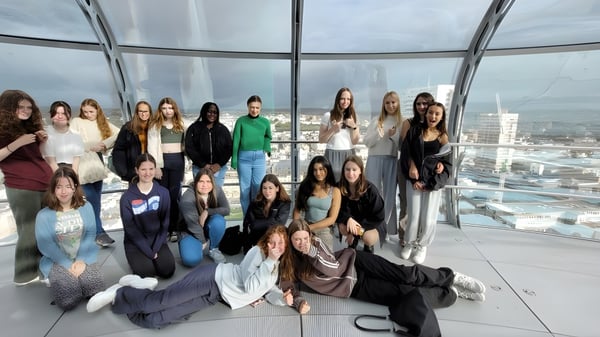 Eine Gruppe Schülerinnen der Brighton Girls School posiert gemeinsam in einem verglasten Raum mit Blick auf die Stadt.