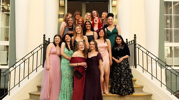 Schülerinnen der Brighton Girls posieren zusammen auf einer Treppe in festlicher Kleidung vor dekorativem Hintergrund.