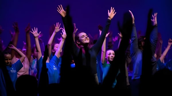Eine Gruppe von Schülerinnen der Brighton Girls hebt die Arme in jubelnder Geste vor dunklem Hintergrund mit violett-blauer Beleuchtung.