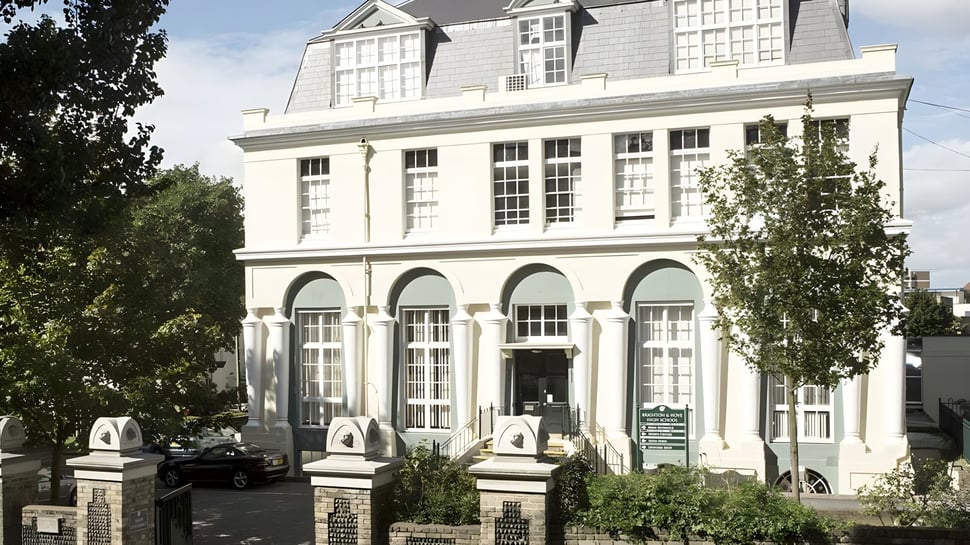 Das historische Schulgebäude der Brighton Girls School mit Bögenfenstern und einer dekorativen Fassade umgeben von Bäumen.