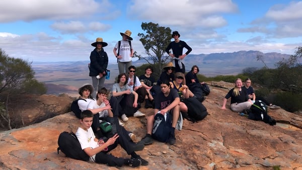 Eine Gruppe von Schülerinnen und Schülern der Brighton Secondary School posiert gemeinsam auf einem Felsen mit Berglandschaft im Hintergrund.