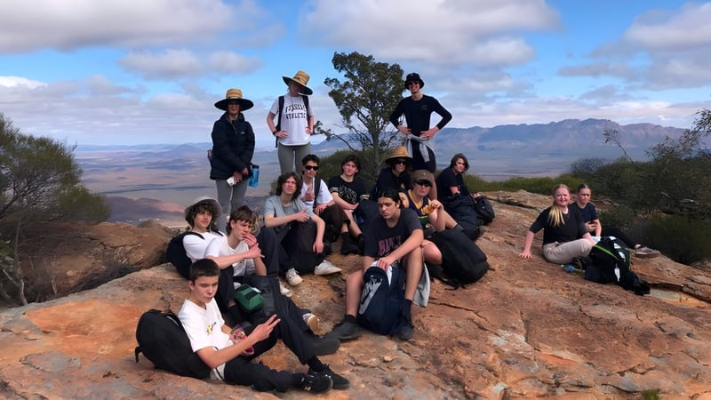Eine Gruppe von Schülerinnen und Schülern der Brighton Secondary School posiert gemeinsam auf einem Felsen mit Berglandschaft im Hintergrund.