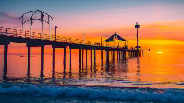 Ein Steg erstreckt sich über ruhiges Wasser vor dem farbenfrohen Sonnenuntergang auf dem Campus der Brighton Secondary School.