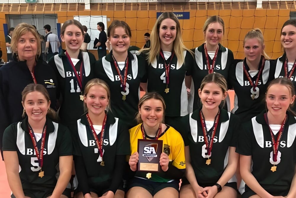 Eine Gruppe junger Volleyballspielerinnen posiert in Uniform auf dem Volleyballfeld der Brighton Secondary School.