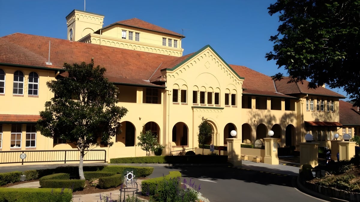 Das eindrucksvolle Hauptgebäude des Brisbane Boys' College steht in einem gepflegten Garten mit Bäumen und einem gepflasterten Weg.