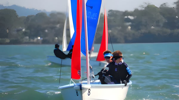 Ein Segelboot mit bunten Segeln auf einem Gewässer vor Bergen und Bäumen auf dem Gelände der Brisbane Grammar School.
