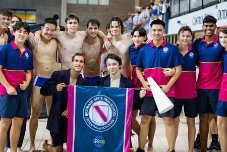 Eine Gruppe von Schwimmerinnen und Schwimmern posiert vor dem Banner der Fédération Internationale de Natation auf dem Campus der Brisbane State High School.