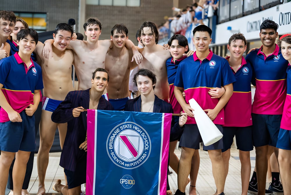 Eine Gruppe von Schwimmerinnen und Schwimmern posiert vor dem Banner der Fédération Internationale de Natation auf dem Campus der Brisbane State High School.
