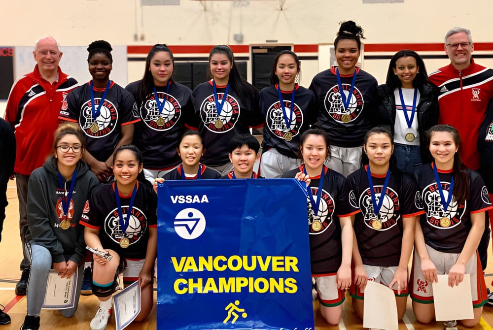 Eine Gruppe junger Athletinnen der Britannia Secondary School hält in einer Sporthalle ein Banner mit der Aufschrift Vancouver Champions.