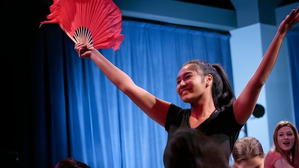 Eine Frau in schwarzem Kleid hält einen roten Fächer und tritt auf der Bühne der British International School Houston auf.