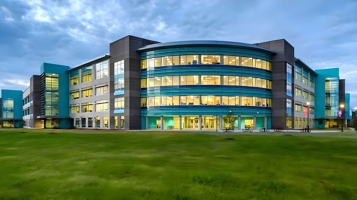 Das moderne mehrstöckige Gebäude der British International School Houston mit einer geschwungenen Glasfassade steht auf einer grünen Wiese vor bewölktem Himmel.
