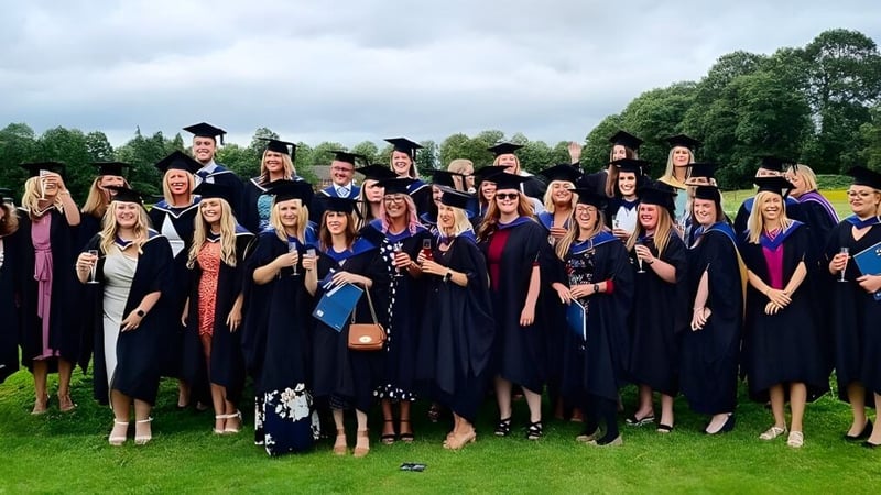 Eine Gruppe von Absolventen steht draußen im Grünen auf dem Campus des Brockenhurst College in akademischer Kleidung.